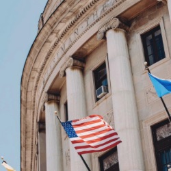 新古典主义政府大楼的特写，有大柱子和石头立面. 几个旗帜, 包括美国国旗, 建筑物前的晴空是否清晰可见.